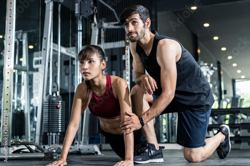 Handsome Caucasian fitness trainer teaching young Asian pretty girl to push up correctly. He setting the position and gesture of the girl in the gym or sport club. Fitness and gym for health concept.