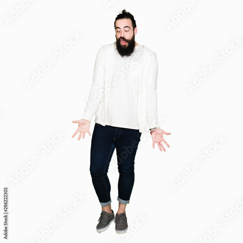 Young man with long hair and beard wearing sporty sweatshirt making fish face with lips, crazy and comical gesture. Funny expression.