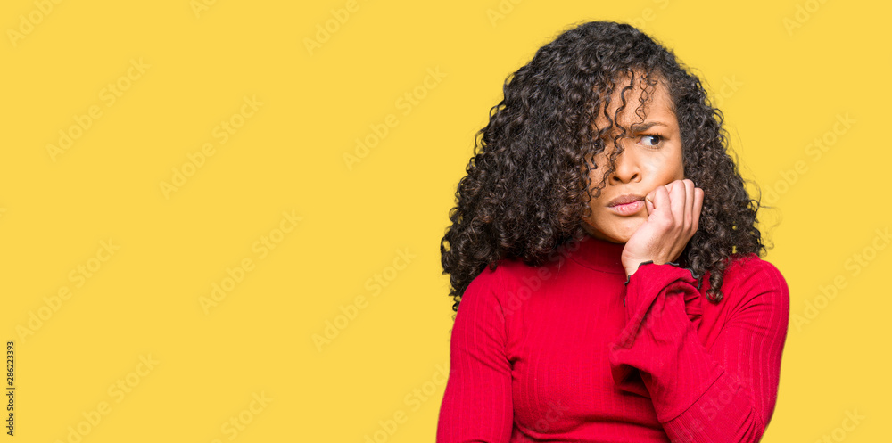 Young beautiful woman with curly hair looking stressed and nervous with hands on mouth biting nails. Anxiety problem. Young beautiful woman with curly hair looking stressed and nervous with hands on mouth biting nails. Anxiety problem.