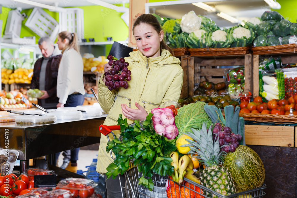 Obraz premium Preteen girl choosing ripe fruits and vegetables in greengrocery