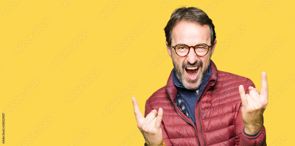Middle age handsome man wearing glasses and winter coat shouting with crazy expression doing rock symbol with hands up. Music star. Heavy concept. Middle age handsome man wearing glasses and winter coat shouting with crazy expression doing rock symbol with hands up. Music star. Heavy concept.