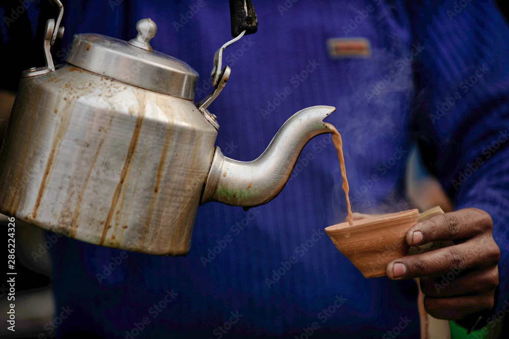Garam chai is Black tea with milk mixed with spices, Pouring tea from the kettle into the clay cup.