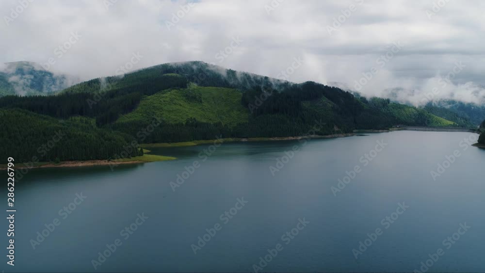 Amazing mountain landscape in nature on foggy weather. The river flows in to the lake in middle of the forest of evergreen trees.