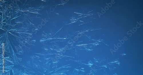 Blue winter background of ice crystals forming and frost freezing on window glass