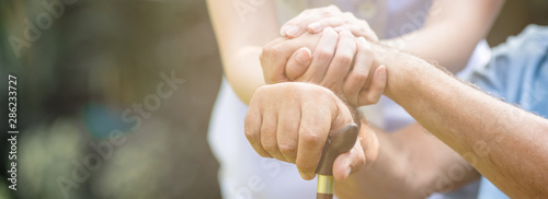 Caring nurse helping senior man sitting on bench in gaden. Asian woman, caucasian man. Holding hands, close up. Web banner frame.