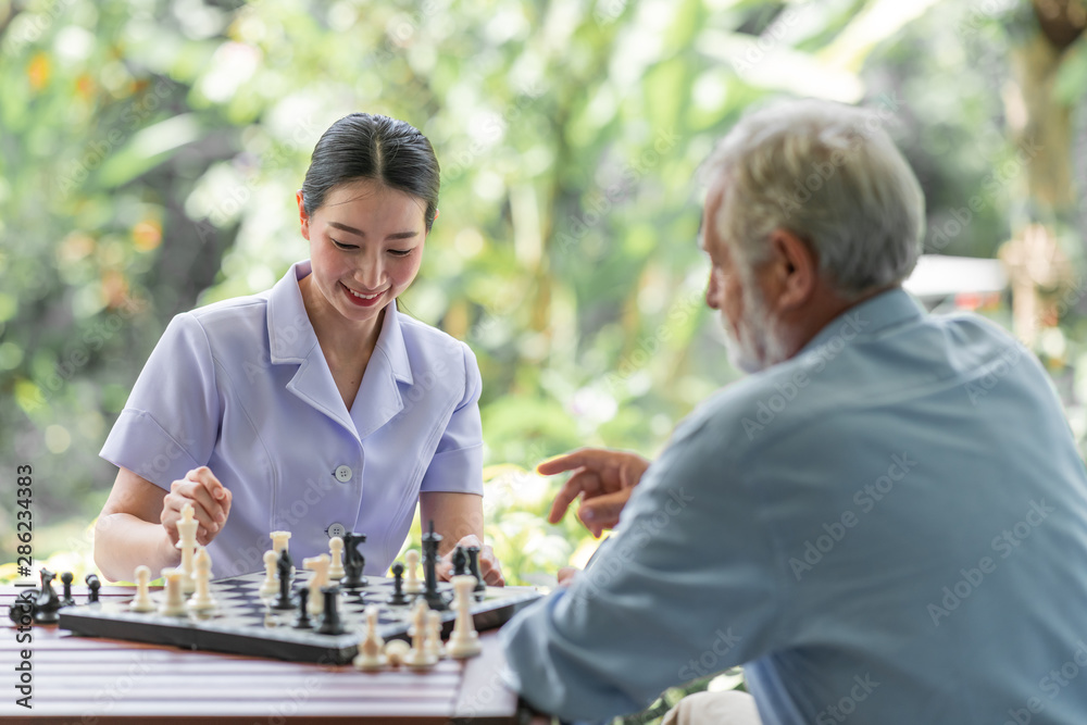 Young nurse playing chess with senior man. White male with asian woman. Happy smile. Young nurse playing chess with senior man. White male with asian woman. Happy smile.