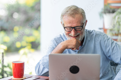 Senior man using laptop sitting on bench in outdoor garden. Caucasian man. Happy laughing mood.