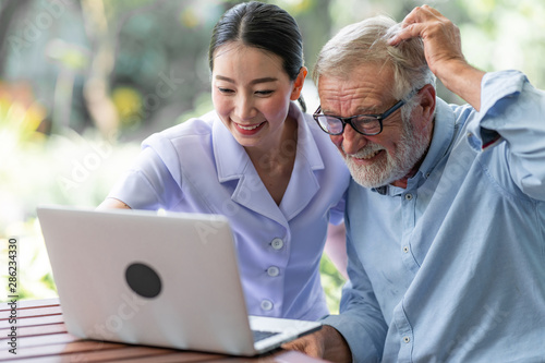 Senior man using laptop with nurse sitting on bench in nursing home. Asian woman and white male. Scraching head. photo