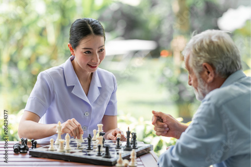 Young nurse playing chess with senior man. White male with asian woman. Concentrating.