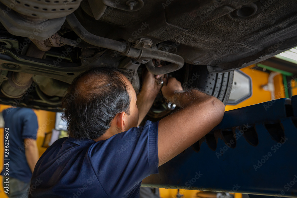 Asian Mechanic repairing a lifted car. Fixing car. Balancing the tire of the car. A car is lifting to let the Asian mechanic diagnostics the suspension of the vehicle to fix or repair it.