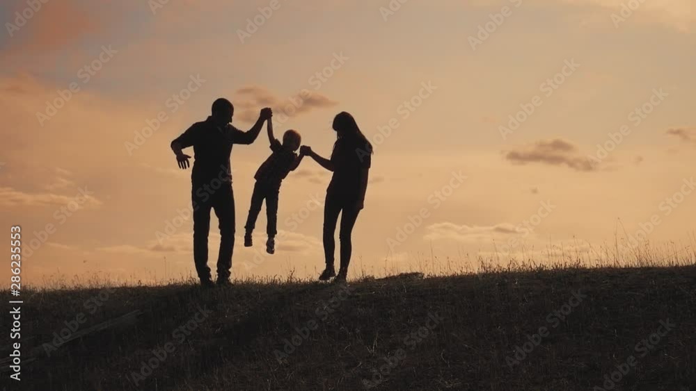 happy family father, mother and son outdoors silhouette concept slow motion video. dad man mom girl hold little boy son by hands. little boy jumping silhouette at sunset lifestyle outdoors. happy