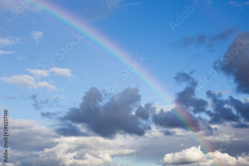 Rainbow and white clouds in blue sky after rain. Nature  travel concept  copy space  soft focus