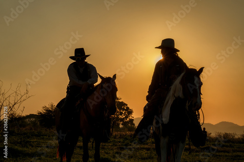 silhouette of cowboys on horseback at sunset