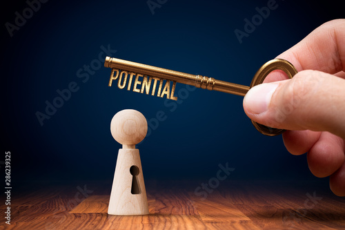 Coach has a key to unlock potential - motivation concept. Coach (manager, mentor, HR specialist) unlock leader potential and talent represented by wooden figurine and hand with key.