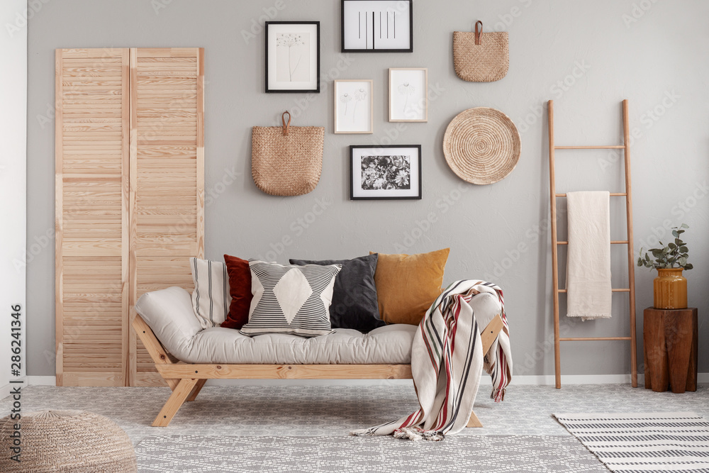 Wooden and wicker accessories in fashionable scandinavian living room interior with futon sofa with pillows - obrazy, fototapety, plakaty 