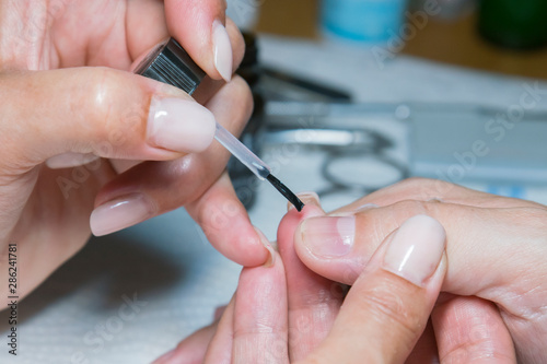 woman hand on manicure treatment with cuticle knife in beauty salon. applying a brush on acrylic nails in the salon