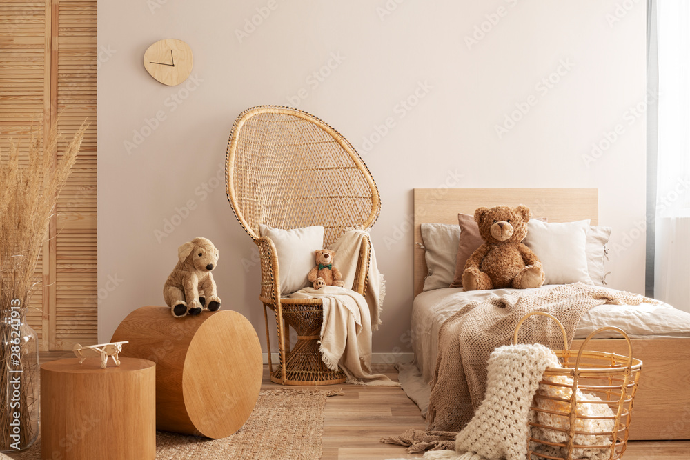 Wicker peacock chair with pillow, armchair and toy in beige and wooden baby bedroom interior - obrazy, fototapety, plakaty 