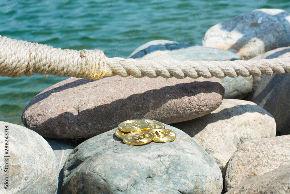 Fototapeta premium Bitcoin on sea stones, in background sea. Concept freelance, stock exchange.Background with copy space for text