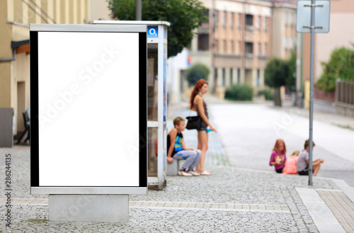 Bilbord reklamowy w centrum miasta, w tle dzieci na chodniku, przystanku autobusowym. 