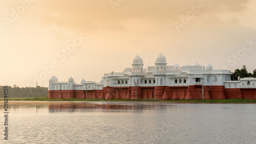 Evening sunset view of the lake place with red and white walls, beautiful domes and archways amid calm and serene water, Tripura, India
