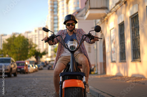 fashionable young man riding a orange motorbike in the street.
