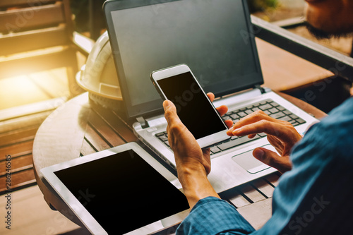 Businessman Holding Mobile smart phone with laptop notebook  tablet on table