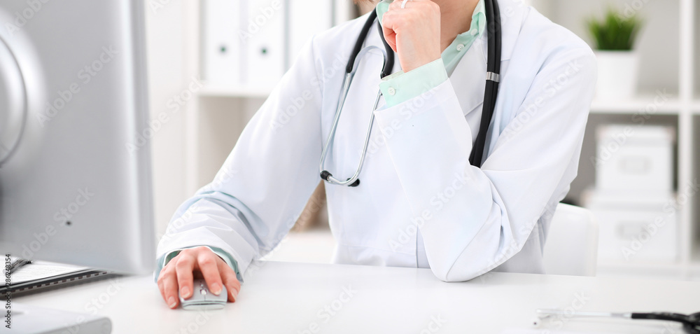 Doctor woman sitting at the desk with computer at workplace in hospital office. Unknown physician's hands close-up. Green tone of blouse. Medicine and health care concept Doctor woman sitting at the desk with computer at workplace in hospital office. Unknown physician's hands close-up. Green tone of blouse. Medicine and health care concept