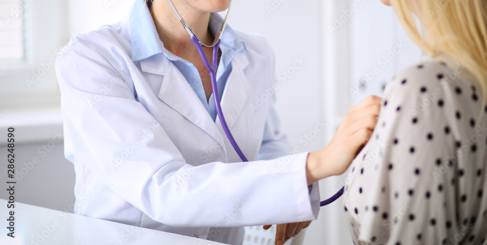 Doctor examining patient with a stethoscope in hospital office. Physician at work. Medicine concept