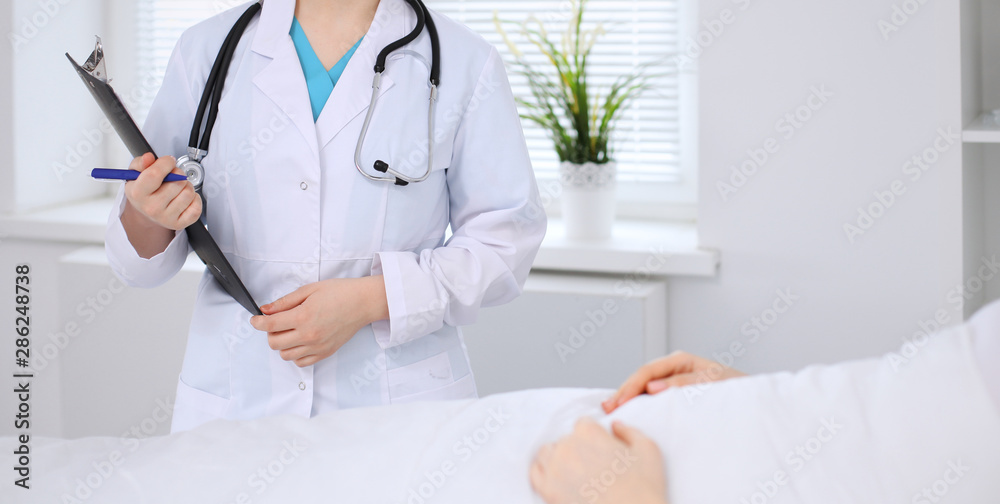 Female doctor filling up application form in hospital ward. Patient lying at the bed and listening physician. Medicine and health care Female doctor filling up application form in hospital ward. Patient lying at the bed and listening physician. Medicine and health care