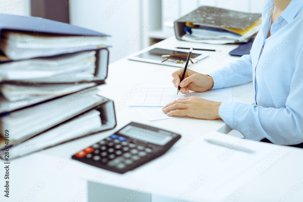Fototapeta premium Unknown female bookkeeper or financial inspector calculating or checking balance, making report, close-up. Internal Revenue Service at work with financial document. Tax and audit concept