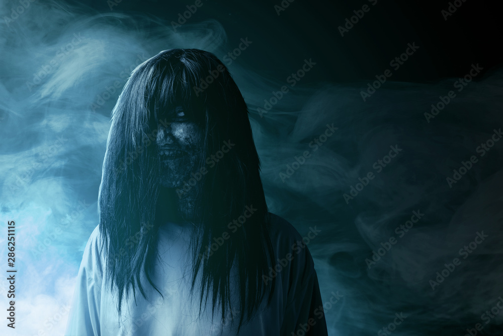 Scary ghost woman with blood and dirty face standing amid the dark fog Scary ghost woman with blood and dirty face standing amid the dark fog