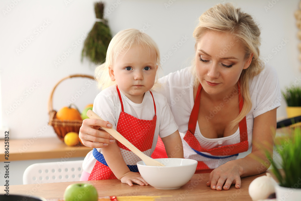 Happy mother and little daughter cooking in kitchen. Spending time all together, family fun concept Happy mother and little daughter cooking in kitchen. Spending time all together, family fun concept