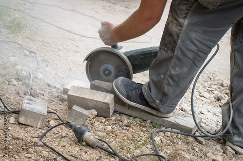 Worker cutting brick with electrical saw for cobblestone pathway, dust surrounding the process
