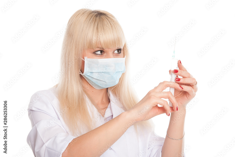 Close-up of a young blonde nurse in a mask looking at a syringe.