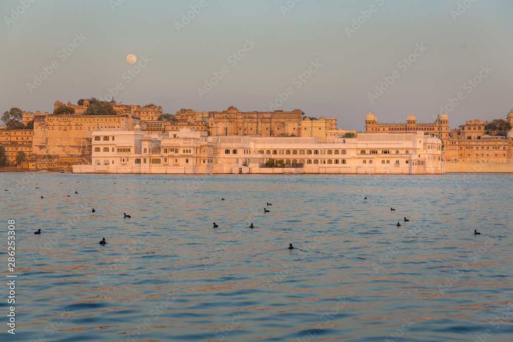 Historic Udaipur City palace on Lake Pichola in Rajasthan, India. . Sunset with view of Full moon