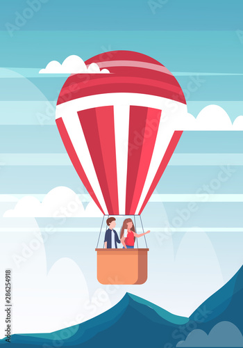 couple flying in basket of hot air balloon man taking photo on smartphone camera woman pointing hand at something travel concept mountains landscape background flat vertical