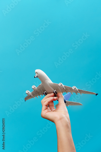 Picture of hand with airplane on empty blue background in studio.