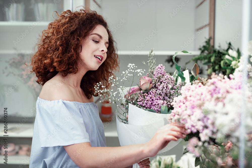 Attractive curly-haired young florist choosing extra flowers for her bouquets Attractive curly-haired young florist choosing extra flowers for her bouquets