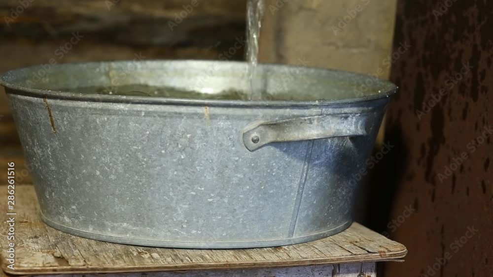 Russian sauna. Interior, inside the bath. Water is pouring from the tap into the pelvis. In the background, a defocused wall made of wooden logs. Russian sauna. Interior, inside the bath. Water is pouring from the tap into the pelvis. In the background, a defocused wall made of wooden logs.
