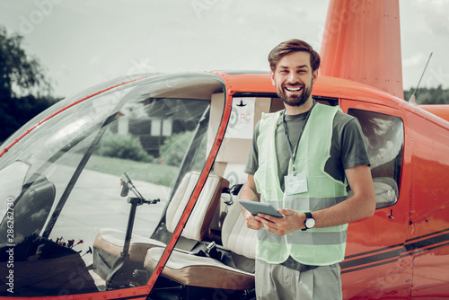 Bearded beaming pilot standing near helicopter after successful flight