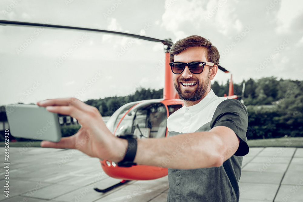 Handsome beaming businessman making selfie near private helicopter