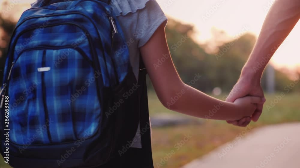 A young man leads his daughter by the hand to school