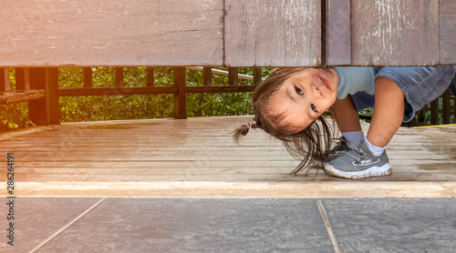 Happy Asian little child girl plays peekaboo under the wooden door in the garden. photo