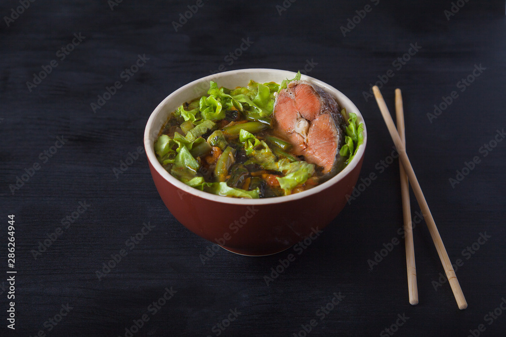 Traditional japanese soup on a red napkin on a black background. A female hand takes out tofu cheese with chopsticks. Copy spaes. Top view. Traditional japanese soup on a red napkin on a black background. A female hand takes out tofu cheese with chopsticks. Copy spaes. Top view.