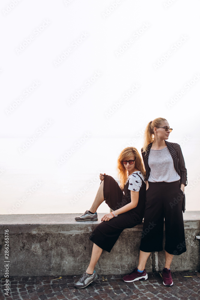 Girls are walking along the promenade on Lake Garda, Italy. Blonde girls in sunglasses are walking on the pier against the background of the lake.