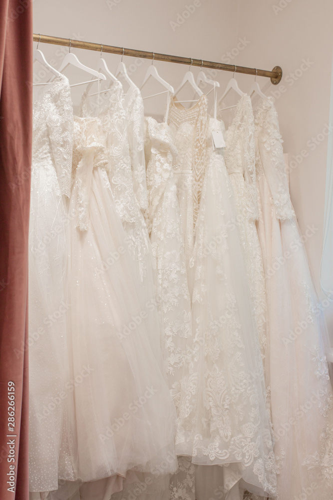Assortment of dresses hanging on a hanger on the background studio. Fashion wedding trends. Interior of wedding shop Assortment of dresses hanging on a hanger on the background studio. Fashion wedding trends. Interior of wedding shop