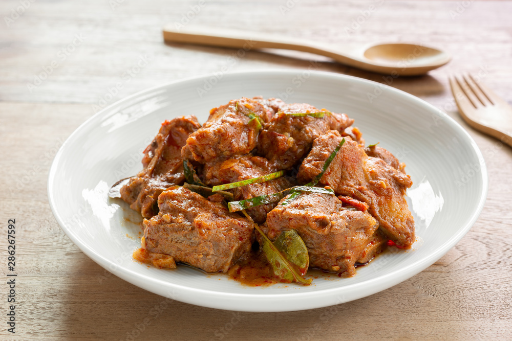 close up of stir fried pork rib with red curry paste in a ceramic dish on wooden table. hot and spicy thai style food menu. close up of stir fried pork rib with red curry paste in a ceramic dish on wooden table. hot and spicy thai style food menu.