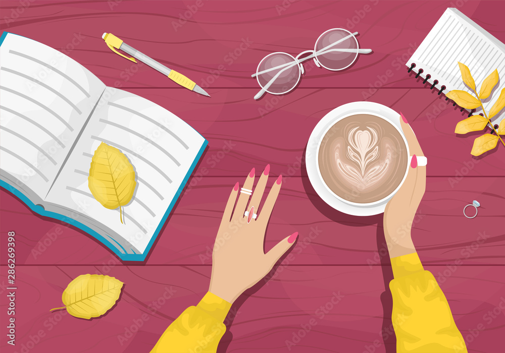 Autumn flat lay background with workplace in a cafe. Women's hands holding a Cup of cappuccino. Burgundy wooden background with yellow autumn leaves. Book, notebook, eye glasses.