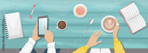 Moody flat lay background with workplace in a cafe. Women's hands holding a Cup of cappuccino and eat cupcake. Light blue wooden background with book, notebook. A man holding a smartphone.