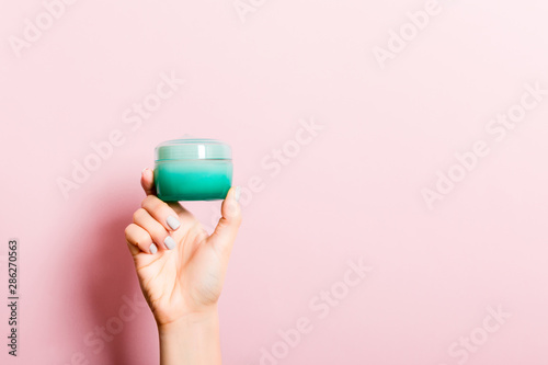 Female hand holding cream bottle of lotion isolated. Girl give jar cosmetic products on pink background